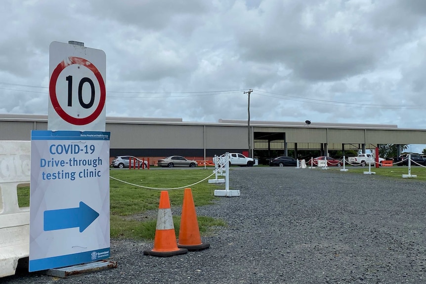 cars line up outside a showground building with a 'covid-19' test sign in the foreground