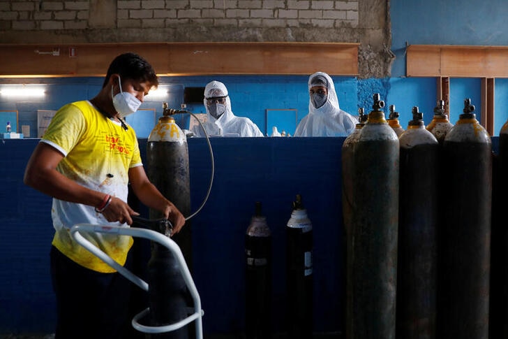 A worker refills an oxygen cylinder as medical workers wait at the Yatharth Hospital in Noida, on the outskirts of New Delhi.