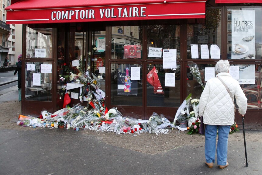 A woman stops to look at flowers, candles and messages in tribute to victims in front of the Comptoir Voltaire cafe, one of the sites of the deadly Paris attacks
