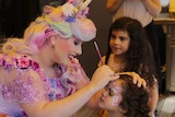 Emily Turnbull is dressed as some kind of unicorn princess and paints a child's face at a party.
