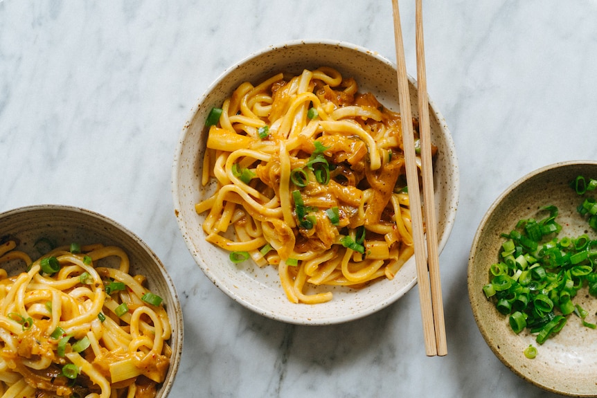 Two bowls of kimchi and cheese udon noodles, with chopsticks and finely sliced spring onions. A fast noodle dinner.