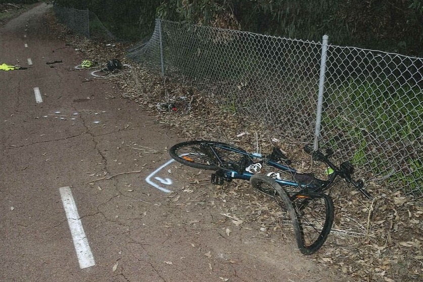 A wrecked bike on a footpath with a large indentation in wire fencing.