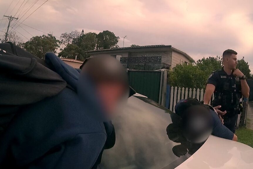 Two youth offenders lay on a car in handcuffs with police nearby