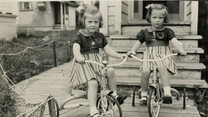 Black and white photo of twin girls on their tricycles
