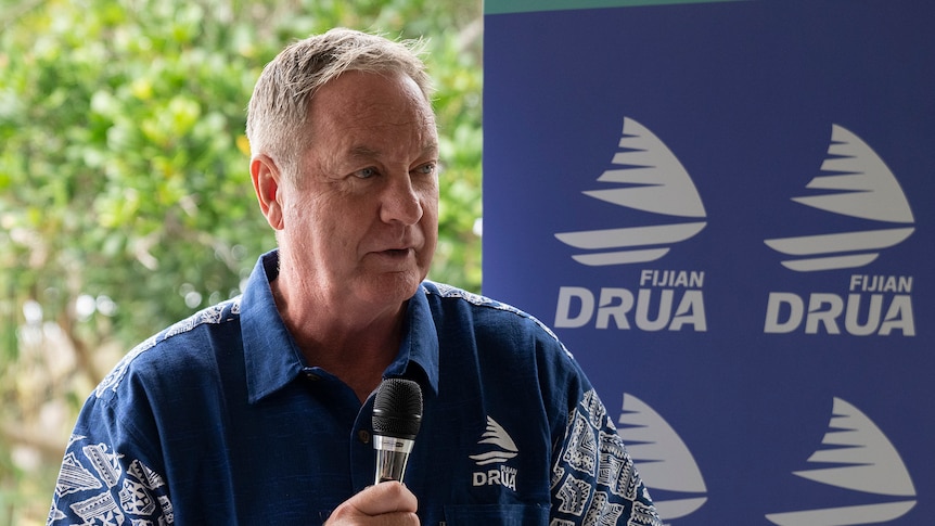 A man stands in front of Fijian Drua signing with a microphone