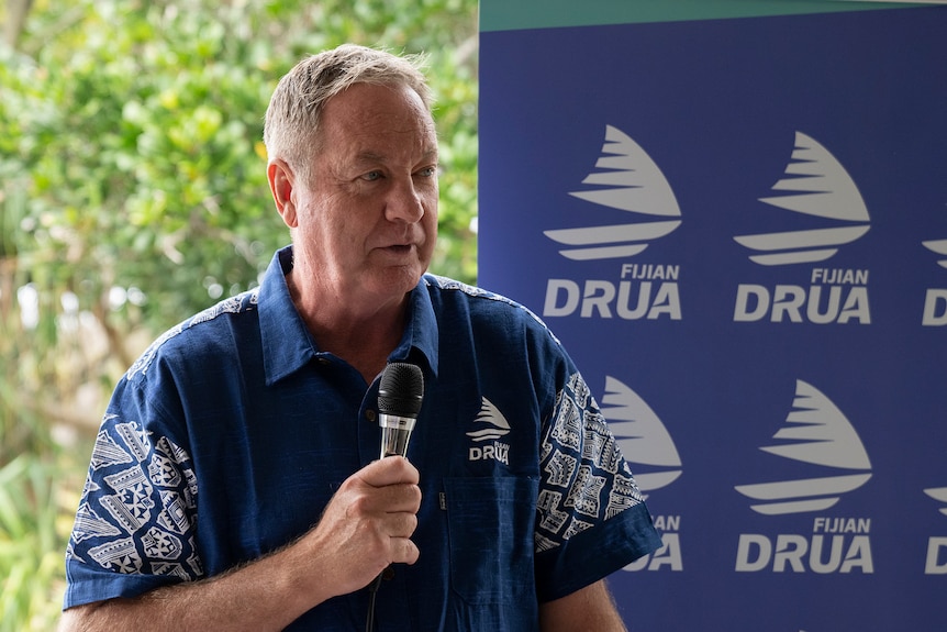 A man stands in front of Fijian Drua signing with a microphone