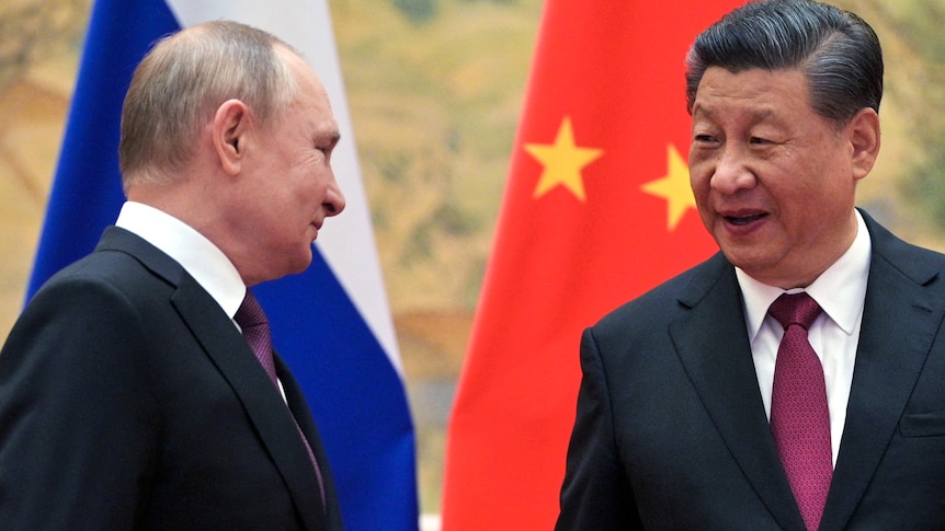 Vladimir Putin smiles as he shakes hands with Xi Jinping in a room lined with flags.