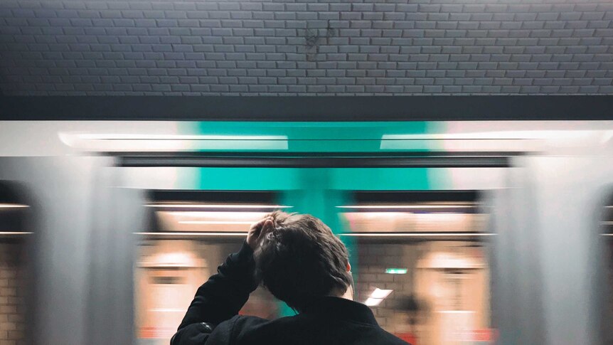A man scratches his head as a train rushes past.