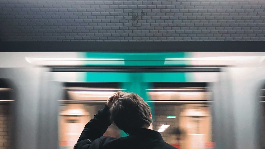 A man scratches his head as a train rushes past. Good generic.