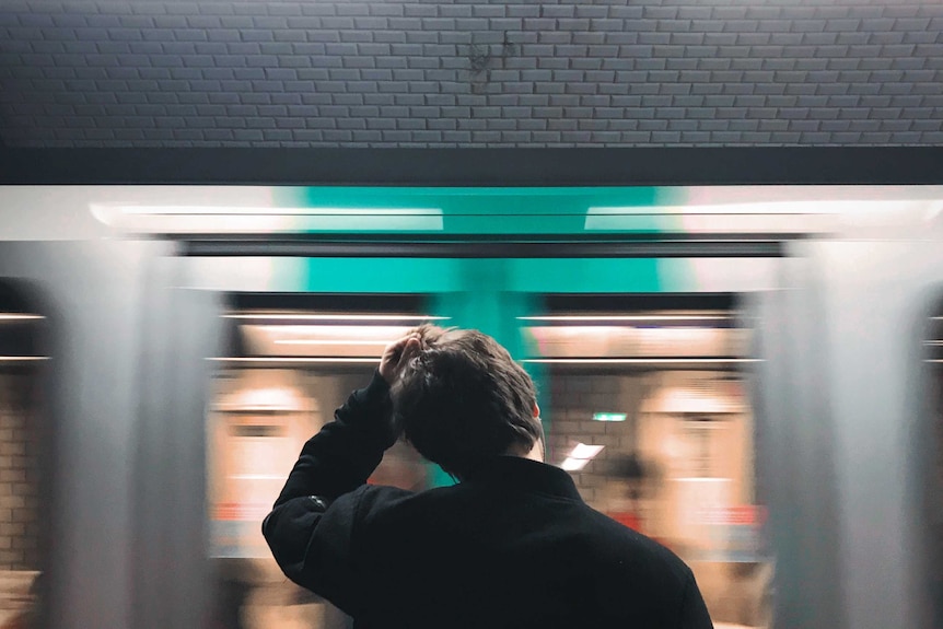 A man scratches his head as a train rushes past.