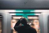 A man scratches his head as a train rushes past.