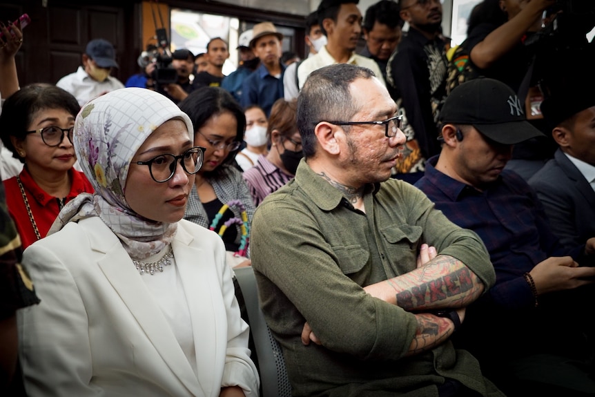 A man and woman sit together in a crowded courtroom 