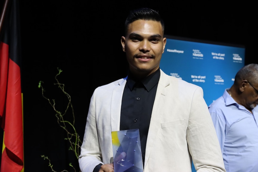 a young man wearing a collared shirt and blazer holding an award