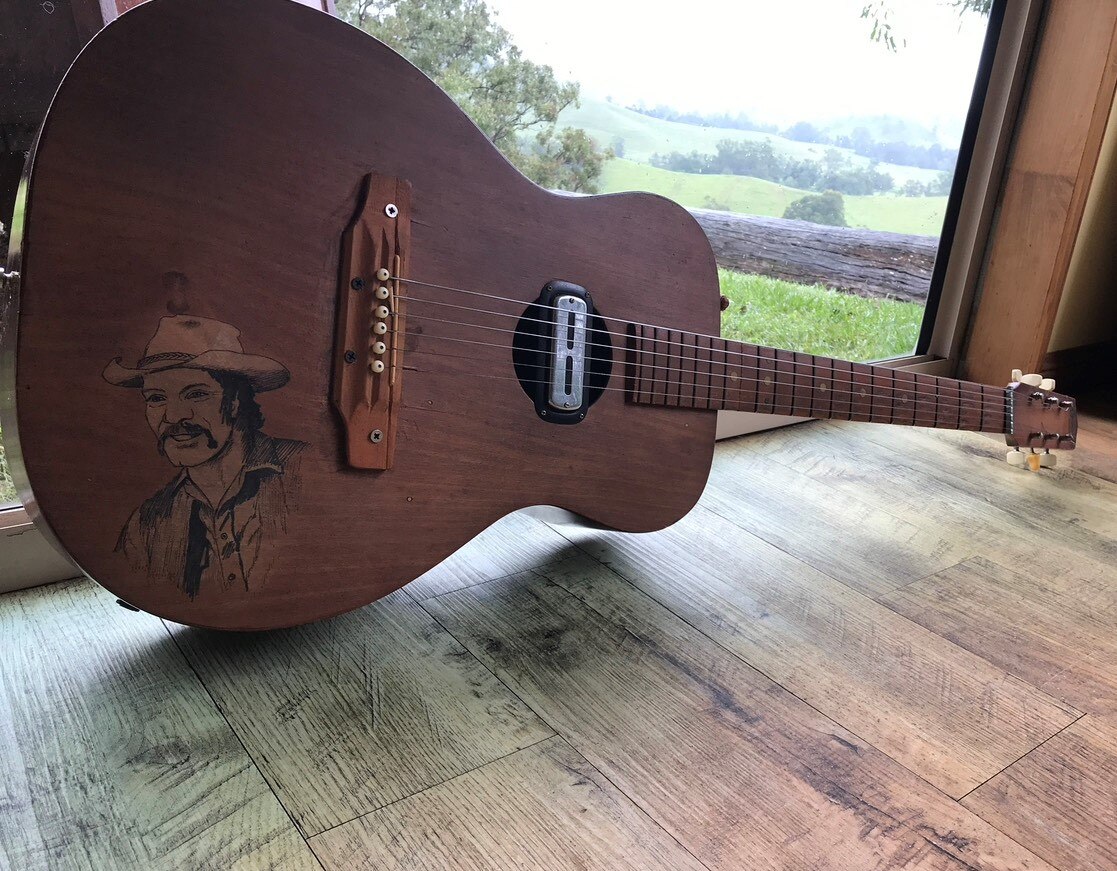 A guitar by a window, with brown wood and a self-portrait on the wood.