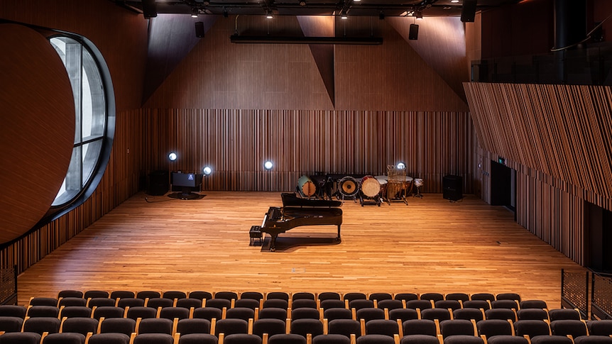 An auditorium with a piano centre-stage and a large round "oculus" window to the left.