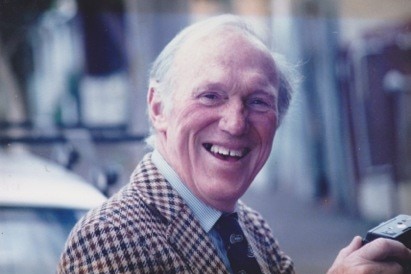 An elderly man in a hound's-tooth jacket and tie.