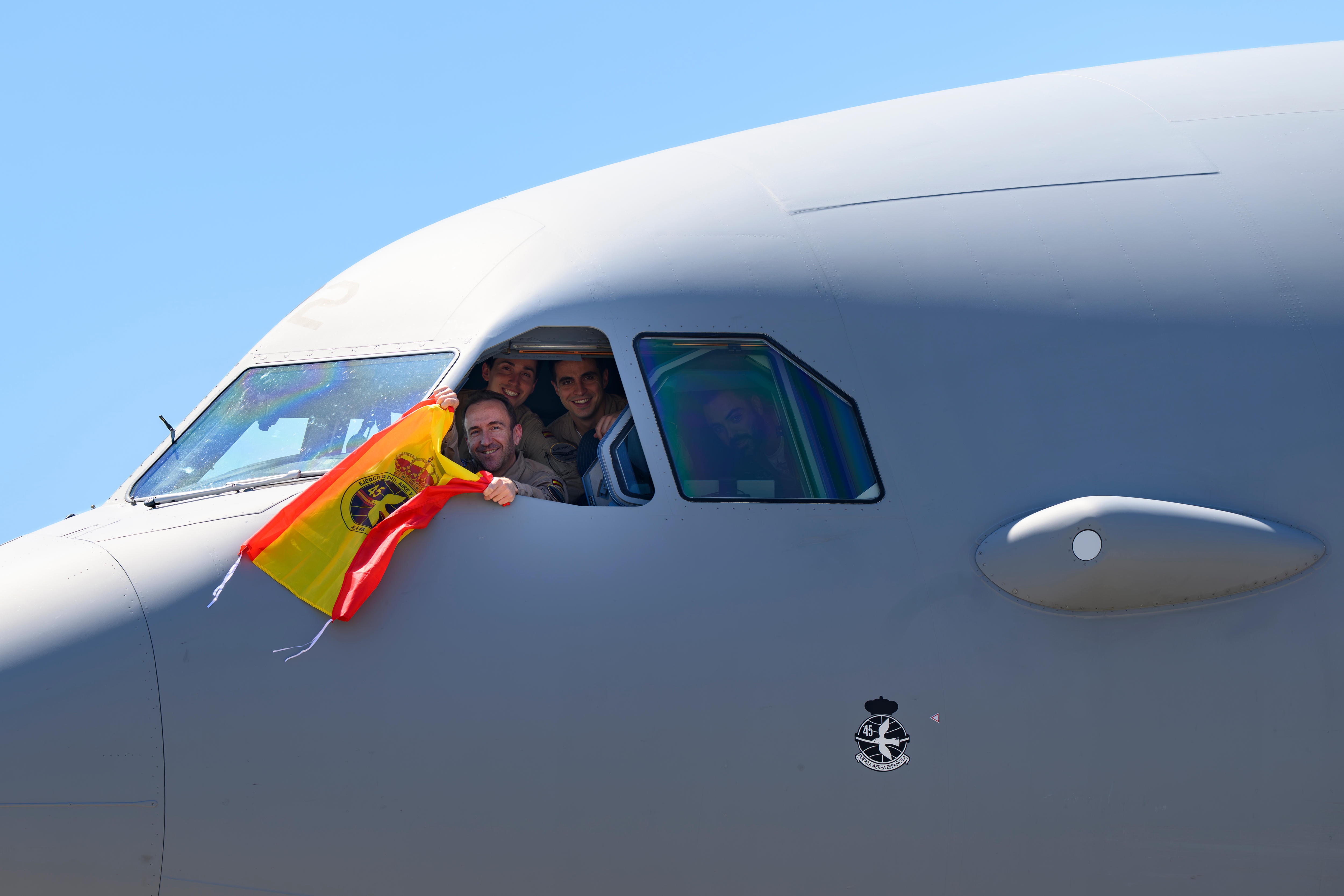 A man holds a Spanish flag out the window of a transport plane.