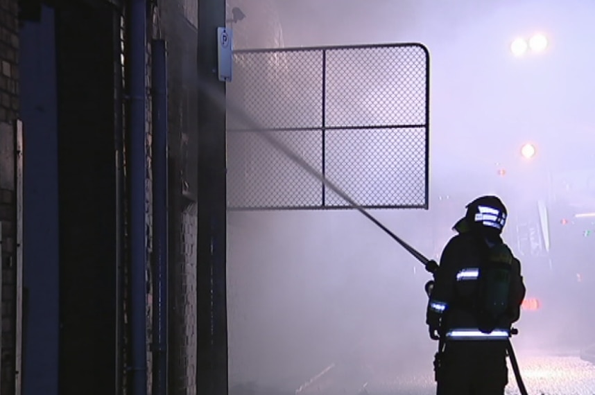 A firefighter uses a hose to extinguish a factory fire.