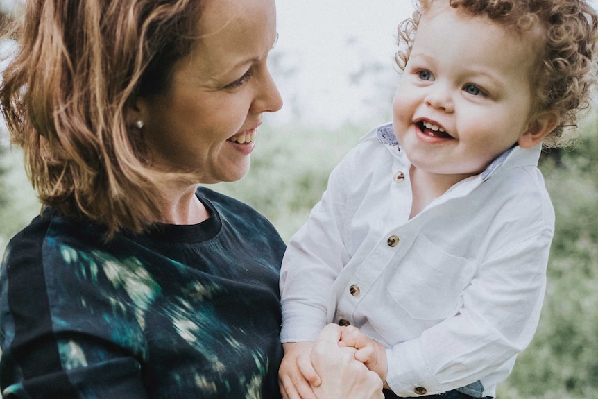 A smiling Taryn Barrett who is holding and looking at son Connor, who's also smiling.