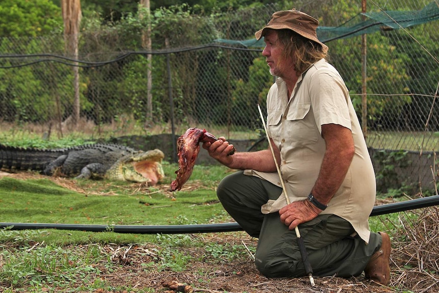 A photo of Trevor Sullivan sitting in an enclosure with his large pet crocodile visible in the background.