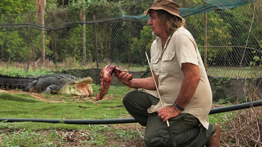 A photo of Trevor Sullivan sitting in an enclosure with his large pet crocodile visible in the background.
