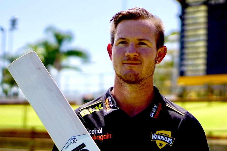 D'Arcy Short holding a cricket bat and wearing a black T-shirt with logos on it at the WACA ground.