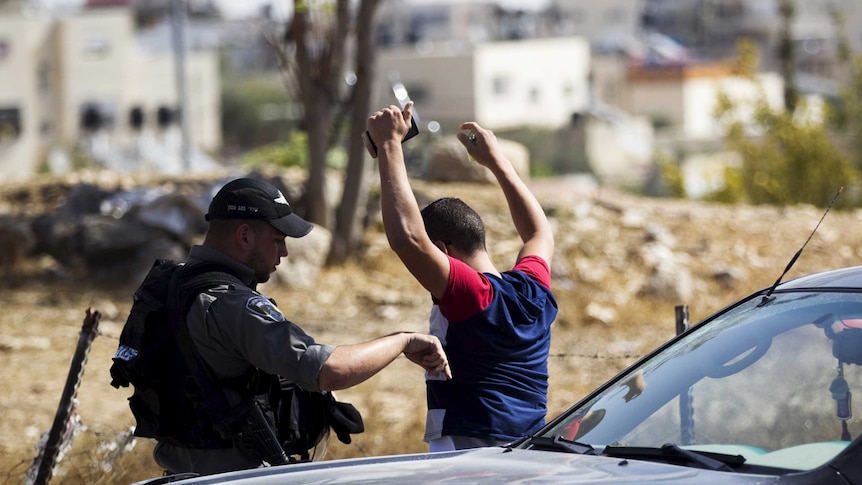 An Israeli policeman performs a security check on a Palestinian man