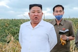 Kim Jong-un in a white shirt standing in a corn field with an aide behind him