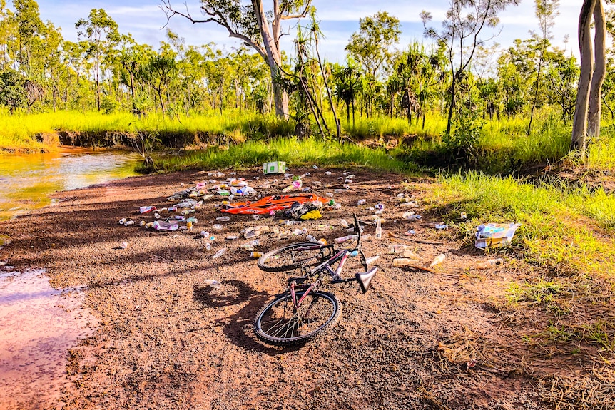 creek bank early morning shadows. red earth, lush trees, lots of bottles, cans, plastic, and a bike