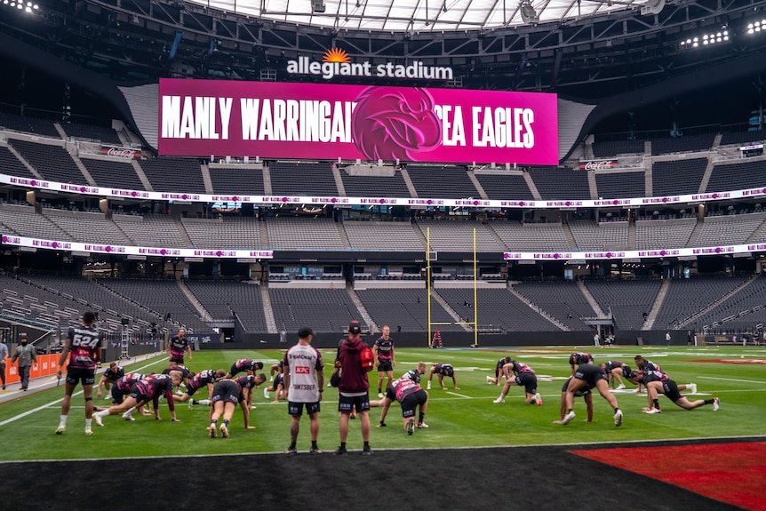 Sea Eagles players train inside a large stadium with 'Manly Warringah Sea Eagles' written on a huge screen.