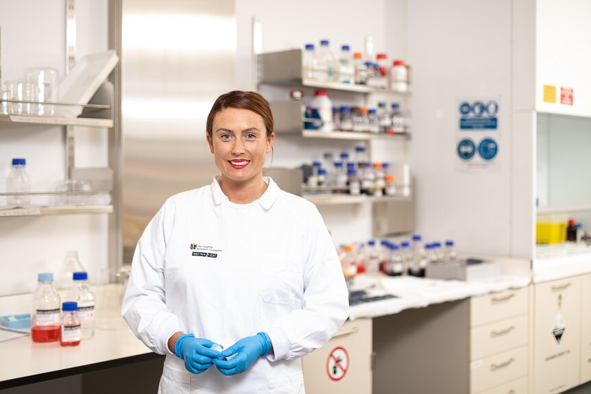 A woman in a lab coat and blue gloves