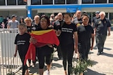 Aboriginals file out of  Launceston airport with remains in box under flag.