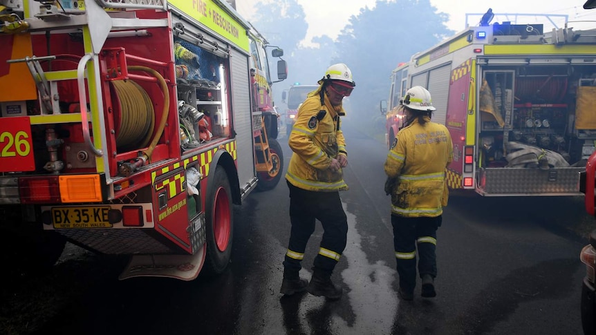 Two firefighters run between two large trucks