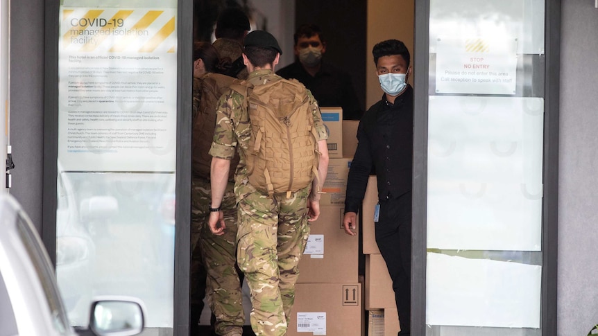 Military personnel in fatigues enter a secure doorway that has been covered with white material to prevent people seeing in.
