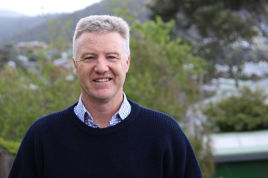 A man with short grey hair and a blue jumper smiles at the camera.