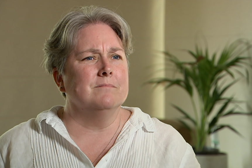 A woman in a white shirt speaks to a TV camera.