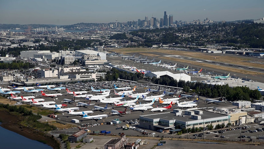 An aerial photo shows the Boeing factory with planes strewn across its runways with the Seattle skyline behind it.