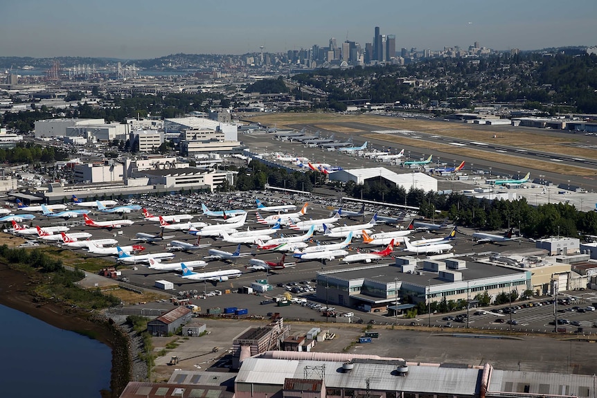 An aerial photo shows the Boeing factory with planes strewn across its runways with the Seattle skyline behind it.