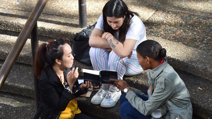 Women from different ethnic backgrounds read the Bible on a street in Sydney.