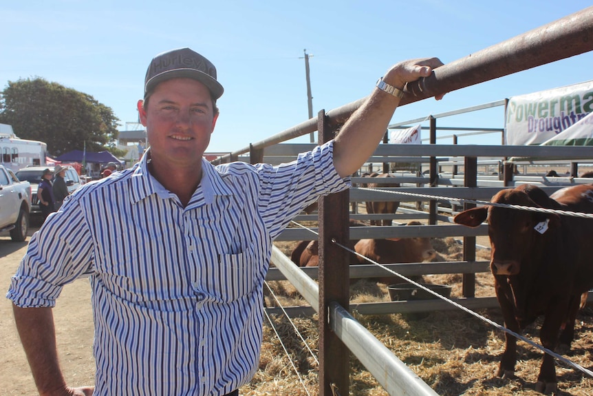 A man in a blue and white striped shirt and a cap standing next to a cattle pen.