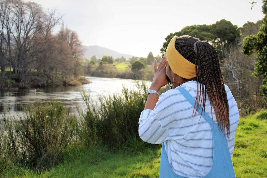 Melanie McCollin-Walker stands on the bank of a river taking a photo.