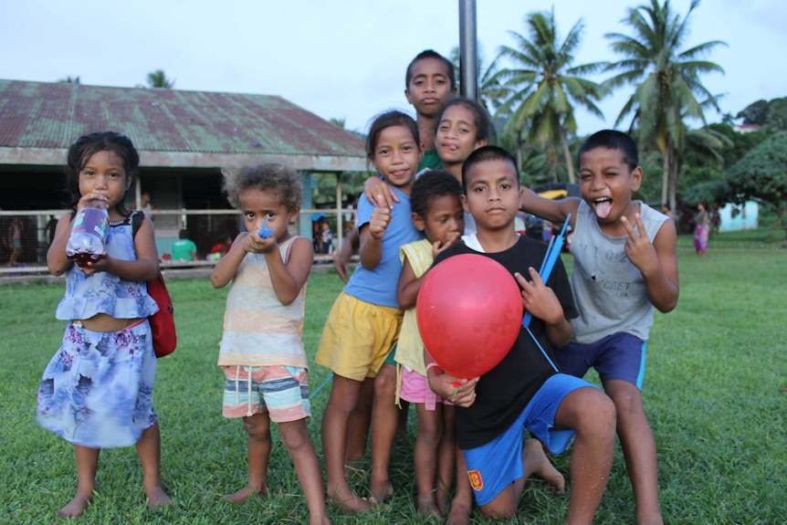 A group of children playing together in front of a house and palm trees on Rabi Island, Fiji.