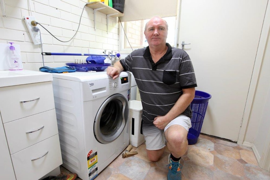 Ray Pilven kneals next to his washing machine.