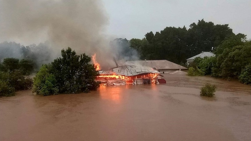 aerial view of a house on fire, surrounded by brown flood waters