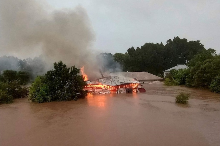 aerial view of a house on fire, surrounded by brown flood waters