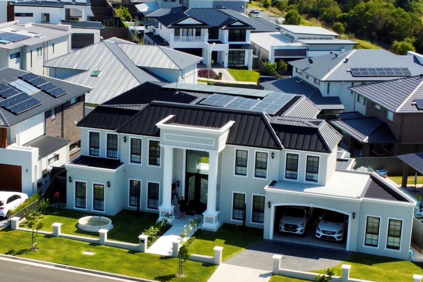 An aerial view of a large newly built house in an estate with an open two car garage and green lawns.