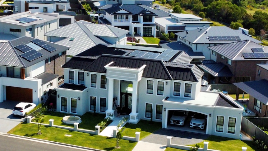 An aerial view of a large newly built house in an estate with an open two car garage and green lawns.