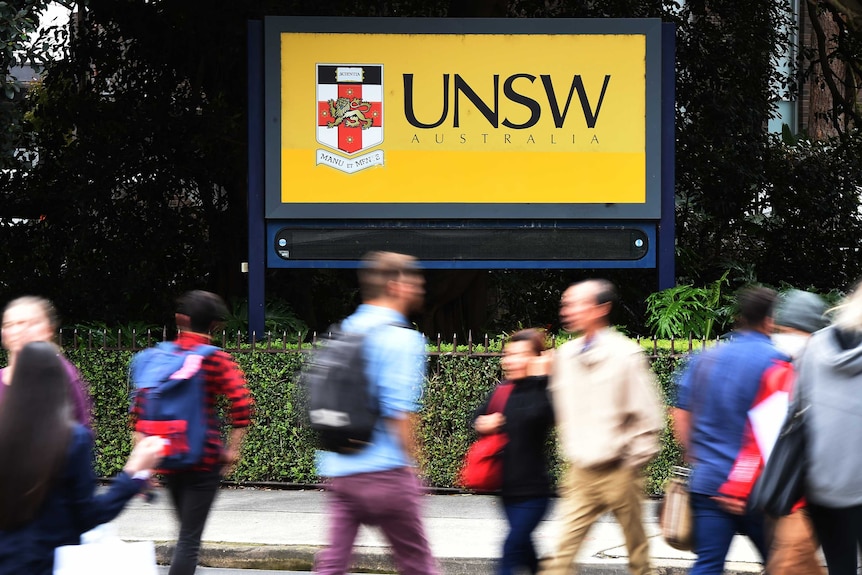 Students walk past a yellow sign that says UNSW