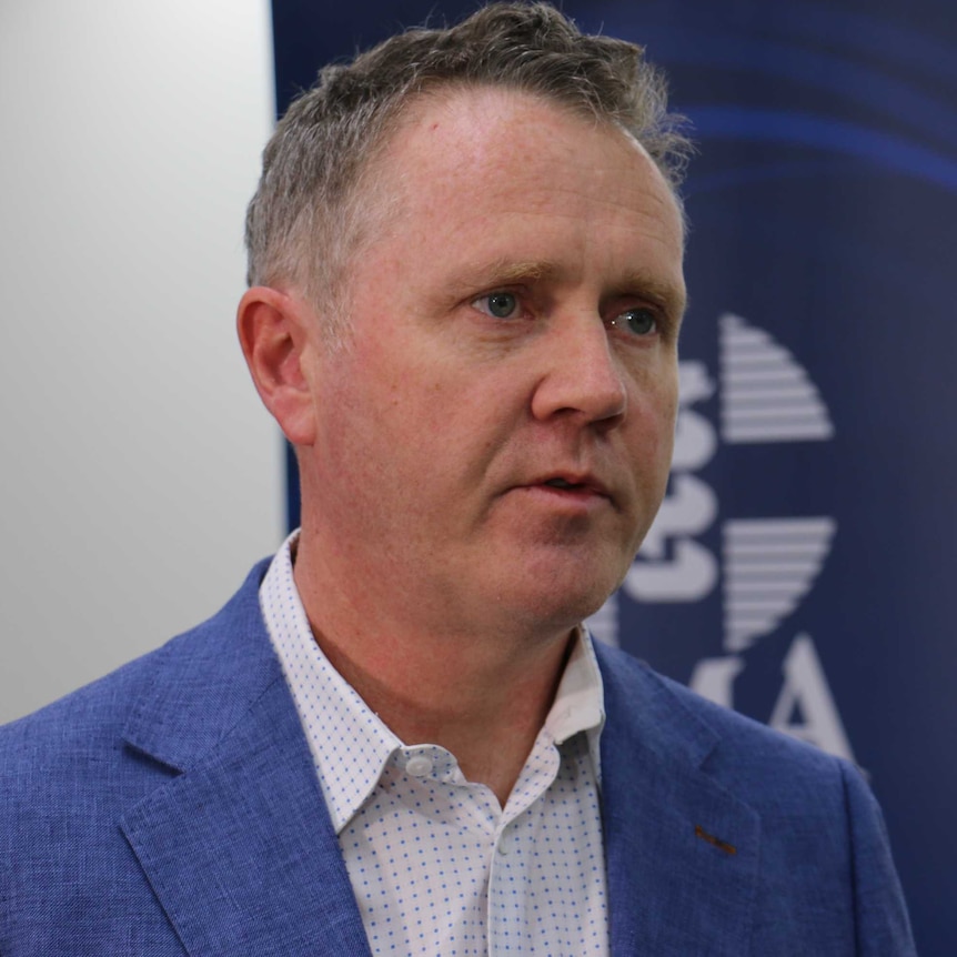 A concerned looking man in the twilight of his middle age wearing a suit of a fashionable blue hue.