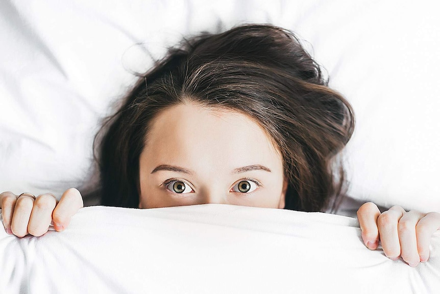 A woman's face partly hidden behind bedclothes
